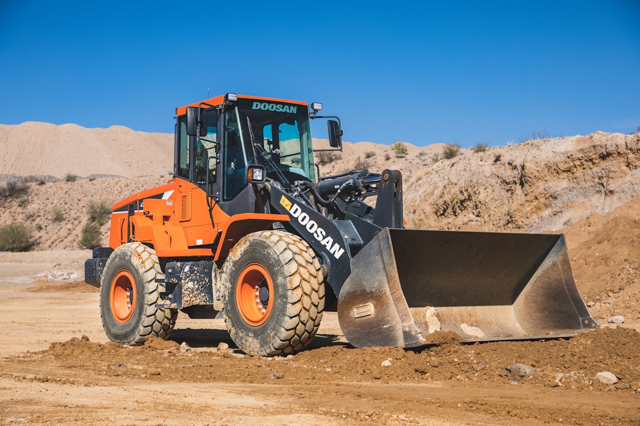 A Doosan excavator working in a sandy rural construction site under a clear blue sky.