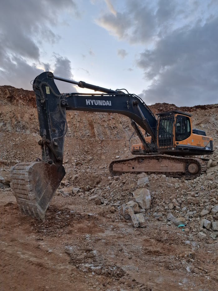 Hyundai excavator working at a rocky construction site under a cloudy twilight sky.
